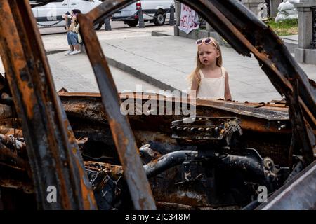 Kiew, Ukraine. 09.. Juni 2022. Ein Mädchen sieht ein verbranntes Auto während einer Ausstellung zerstörter ukrainischer Bürgerwagen und russischer Kriegsfahrzeuge, die am 9. Juni 2022 auf dem Michailovskyi-Platz in der Altstadt von Kiew, Ukraine, ausgestellt wurden. Als die Russische Föderation vor 3 und einem halben Monat in die Ukraine einmarschierte, dauern die heftigen Kämpfe im Osten des Landes an. Die Hauptstadt Kiew bleibt in relativer Sicherheit, obwohl in der ganzen Stadt Erinnerungen an den Krieg wie schützende Sandsäcke, Straßensperren, nationale und Anti-Kriegs-Symbole zu sehen sind. (Foto von Dominika Zarzycka/Sipa USA) Quelle: SIPA USA/Alamy Live News Stockfoto