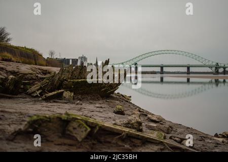 Schiffswrack am Sandstrand, Wigg Island, mit der Runcorn Bridge / Silver Jubilee Bridge im Hintergrund - Runcorn, Großbritannien. Stockfoto