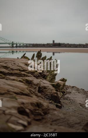 Schiffswrack am Sandstrand, Wigg Island, mit der Runcorn Bridge / Silver Jubilee Bridge im Hintergrund - Runcorn, Großbritannien. Stockfoto