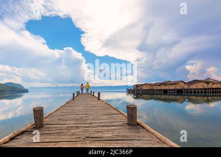 Hölzerner Pier und Wolkenlandschaft mit einem Paar am Ende des Docks in der Bucht, die als Knochenbucht im Ohridsee, Mazedonien, bekannt ist. Stockfoto