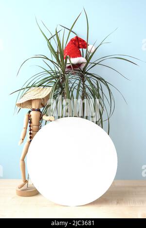 Weihnachten im Juli weiß rund Zeichen mockup im Urlaub Sommer Strand Hintergrund. Sommerurlaub. Party Dekoration mit Holzfigur eines Mannes in einem wic Stockfoto