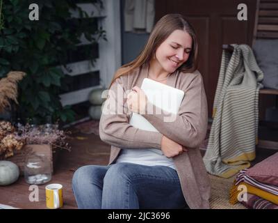 Emotionale Frau mittleren Alters studiert zu Hause mit Laptop. Freut sich über gute Nachrichten, Frau liest E-Mail oder Social-Media-Nachricht, gewinnt Online-Lotterie, großes Shopping-Angebot, sitzt auf Veranda zu Hause Stockfoto