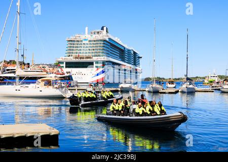 Touristen besetzen aufblasbare Boote für eine schnelle Fahrt auf den Fjorden. Alle sind in Hi-viz Jacken. P & O Cruises MS Iona liegt an den Kais Stockfoto