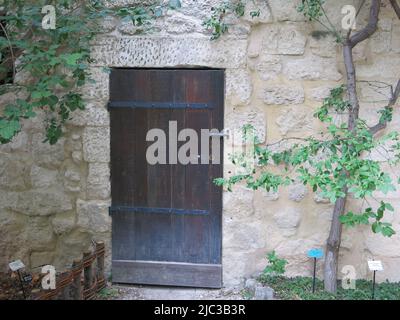 Eine alte hölzerne Tür in einer Steinmauer - die zu einem geheimen Garten führt? Der Jardin Medieval in Uzes in Frankreich liegt auf dem Gelände der Burg Raynon. Stockfoto