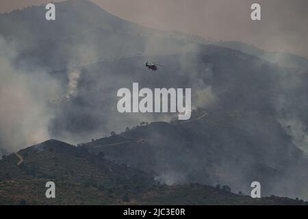 Malaga, Spanien. 09.. Juni 2022. Allgemeiner Blick auf Rauch, der während eines Waldbrands in Pujerra über die Berge steigt, während ein Hubschrauber fliegt. Rund fünfhundert Waldarbeiter von INFOCA (andalusischer Waldfeuerlöschdienst) und weitere hundert von militärischen Notdiensten kämpften gegen Flammen, um einen Waldbrand zu löschen, der am 8.. Juni aufgrund hoher Temperaturen und komplizierter aerographischer Bedingungen ausbricht. Als Reaktion darauf wurden 3,000 Bewohner des Dorfes Benahavis aus ihren Häusern in andere Einrichtungen evakuiert. Kredit: SOPA Images Limited/Alamy Live Nachrichten Stockfoto