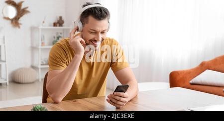 Schöner Mann mit Smartphone und Kopfhörer, der am Tisch Musik hört Stockfoto