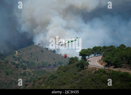 Allgemeiner Blick auf Rauch, der während eines Waldbrands in Pujerra über die Berge steigt, während ein Hubschrauber fliegt. Rund fünfhundert Waldarbeiter von INFOCA (andalusischer Waldfeuerlöschdienst) und weitere hundert von militärischen Notdiensten kämpften gegen Flammen, um einen Waldbrand zu löschen, der am 8.. Juni aufgrund hoher Temperaturen und komplizierter aerographischer Bedingungen ausbricht. Als Reaktion darauf wurden 3,000 Bewohner des Dorfes Benahavis aus ihren Häusern in andere Einrichtungen evakuiert. (Foto von Jesus Merida/SOPA Images/Sipa USA) Stockfoto