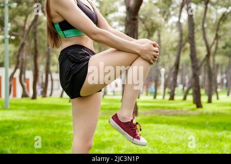 Junge Brünette Frau trägt sportliche Kleidung im Stadtpark, Outdoor-Läufer Athlet Frau tun Fitness-Stretch. Ein Bein halten, um Hamstr Stockfoto