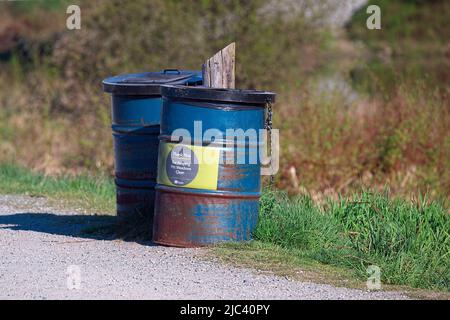 Blaue Metallabfallbehälter, die an einen Pfosten entlang eines Erholungsweges gekettet werden. Stockfoto