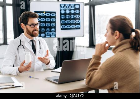 Ein aufmerksamer, kluger kaukasischer Arzt der Allgemeinmedizin konsultiert eine Patientin in einer Arztpraxis, gibt Empfehlungen, verschreibt eine Behandlung, beantwortet Fragen und lächelt Stockfoto