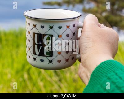 Hände halten Teetasse auf grünem Bokeh Hintergrund. Frau mit einer Tasse Tee. Unscharfer, selektiver Fokus. Stockfoto