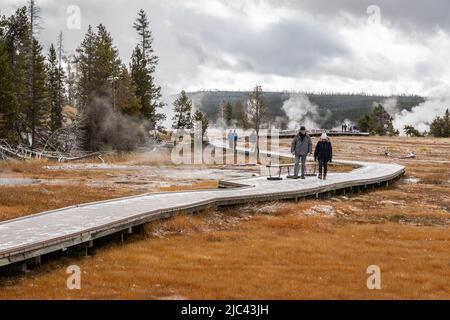 Yellowstone, Wyoming, USA - 3. Oktober 2019: Touristen, die auf der Promenade spazieren gehen, um das Geysir-Becken mit Rauch- und Dampfschwaden zu besichtigen Stockfoto
