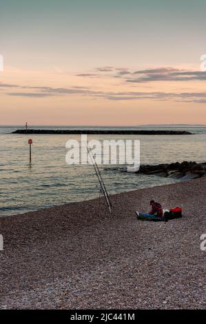 Ein einmunter Fischer am Strand in der Abenddämmerung, Sidmouth, East Devon, England Stockfoto