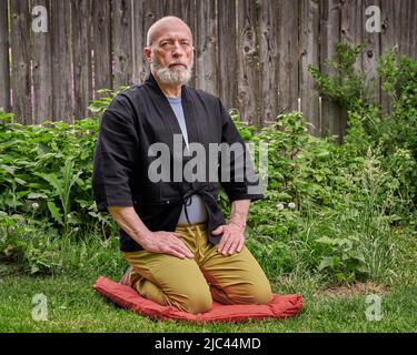 Kopf- und Schulterporträt eines kahlen und bärtigen älteren Mannes, der einen kurzen Kimono trägt und in einer traditionellen japanischen Seiza-Position auf einem Kissen pa sitzt Stockfoto