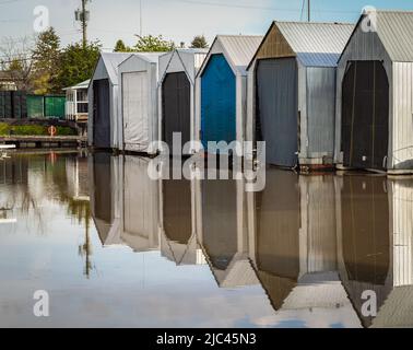 Bunte Bootshäuser auf einem Fluss. Am frühen Morgen Sonnenlicht auf der Werft, Marina. Schwimmende Bootsgaragen auf einem Wasser. Straßenfoto, niemand, selektiver FOC Stockfoto