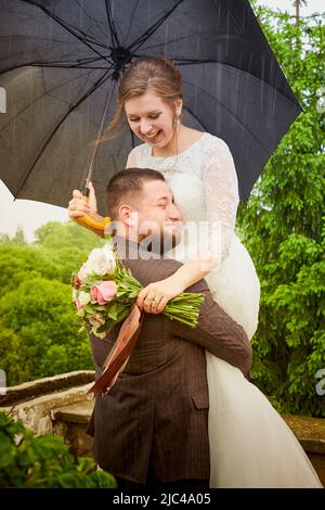 Das Brautpaar spaziert an einem grünen Sommertag mit einem Regenschirm im grünen Park Stockfoto