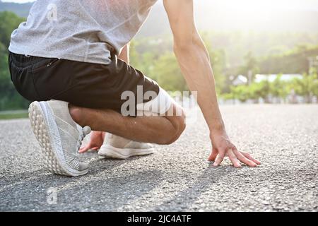 Ein männlicher Athlet in einer Sportkleidung, der sich auf der Straße entlang des grünen Parks zum Joggen vorbereitet. Lauf- oder Joggingkonzept. Zugeschnittenes Bild, Rückansicht Stockfoto