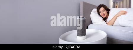 Lächelnden jungen Frau liegend auf Bett Musik auf kabellose Lautsprecher Stockfoto