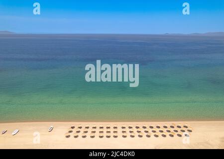 Blick auf den Strand von einer Drohne aus gesehen auf gerade Reihen von Sonnenschirmen und die Oberfläche des Meeres Stockfoto