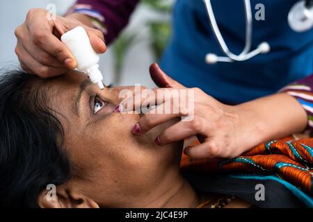 Krankenschwester oder Arzt tropft Augentropfen auf schlafende kranke Frau mittleren Alters auf dem Bett - Konzept der Therapie, Behandlung und medizinische Unterstützung Stockfoto