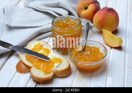 Pfirsichmarmelade in einer Glasschüssel mit Löffel, Brotscheibe und Pfirsichen Stockfoto