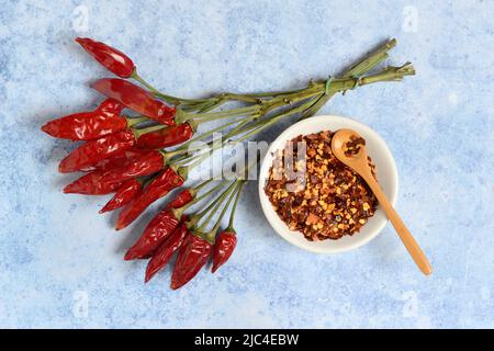 Getrocknete Chili-Paprika (Capsicum annuum) in der Büschel und Chili-Flocken in der Schüssel Stockfoto
