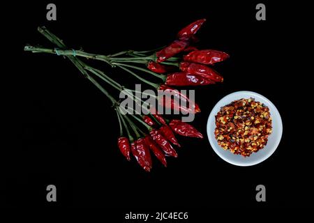 Getrocknete Chili-Paprika (Capsicum annuum) in der Büschel und Chili-Flocken in der Schüssel Stockfoto