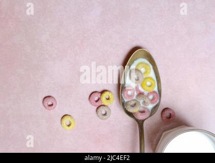 Müsli-Ringe mit Fruchtgeschmack in Löffel und Glas Milch, Kinderfrühstück, Müsli Stockfoto