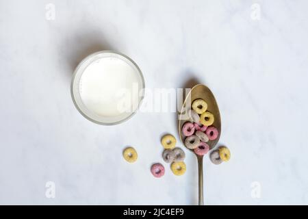 Müsli-Ringe mit Fruchtgeschmack in Löffel und Glas Milch, Kinderfrühstück, Müsli Stockfoto