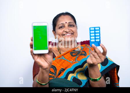 Lächelnde Frau zeigt Green-Screen-Handy mit Medikamenten oder Pillenband, indem sie Kamera auf isolierten Hintergrund - Konzept der Online-App-Bestellung und Stockfoto