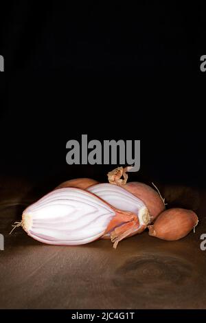 Halbgebackene Zwiebel (Allium cepa var. aggregatum), auf einem Holztisch, Food-Fotografie mit schwarzem Hintergrund Stockfoto