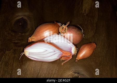 Halbgebackene Zwiebel (Allium cepa var. aggregatum), auf einem Holztisch, Food-Fotografie mit schwarzem Hintergrund Stockfoto