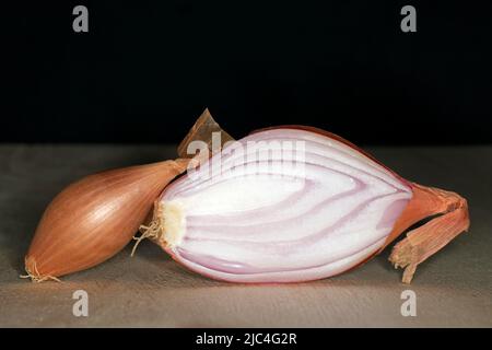 Halbgebackene Zwiebel (Allium cepa var. aggregatum), auf einem Holztisch, Food-Fotografie mit schwarzem Hintergrund Stockfoto