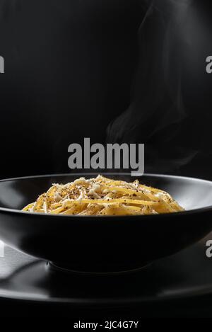 Italienische Pasta auf schwarzem Teller. Heiße Pasta kommt dampfend aus dem gekochten Gericht. Cacio e Pepe – Italienische Pasta Stockfoto