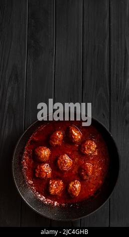 Fleischbällchen auf einem Grill in Tomatensauce auf schwarzem Hintergrund Draufsicht Kopierraum. Vertikale Aufnahmen Stockfoto