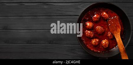 Skandinavische Küche. Fleischbällchen in Soße in einer gusseisernen Pfanne auf schwarzem Hintergrund Draufsicht Kopierraum. Stockfoto