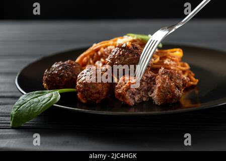 Italienische Pasta mit Fleischbällchen und Tomaten und Basilikumsoße. Eine Gabel fädelt den Fleischball Stockfoto