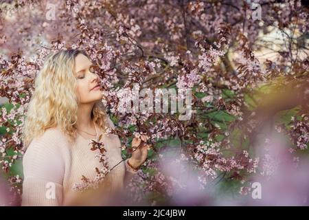 Portrait einer blonden lächelnden unbeschwerten Frau in großen, schönen Fliederblumen, die wie ein Baum verzweigen. Geruch von Pflanzen als Allergie Stockfoto