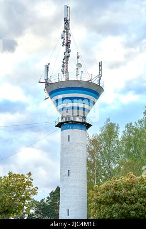 Weißer Ziegelwasserturm mit drahtloser Kommunikationsantenne Sender gegen blauen Himmel und Bäume.Internet, 3G, 4G und 5G Mobilfunkverbindung. Stockfoto