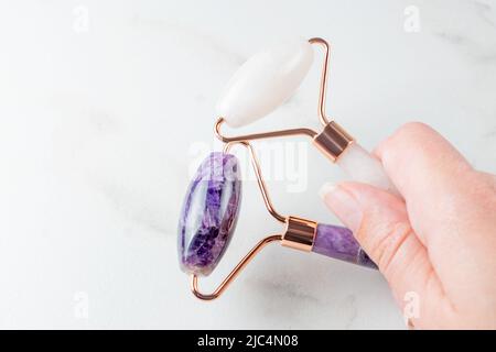 Weibliche Hand, die zwei Massagerollen aus Stein hält. Rosenquarz Jade Walze. Hautpflege zu Hause, Anti-Aging- und Lifting-Therapie. Stockfoto