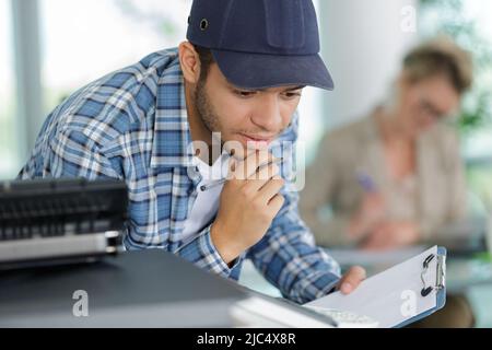 Junger Mann, der in einem Büro einen Fotokopierer bedient Stockfoto