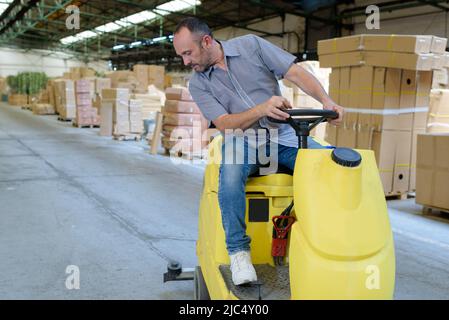 Mann reinigt das Lager mit einer Auffahrmaschine Stockfoto