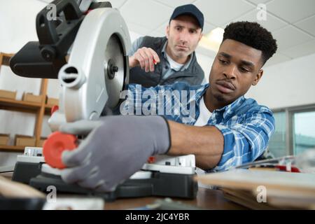 Der Meister erklärt die Arbeit an der Gehrungsäge in der Zimmerei Stockfoto