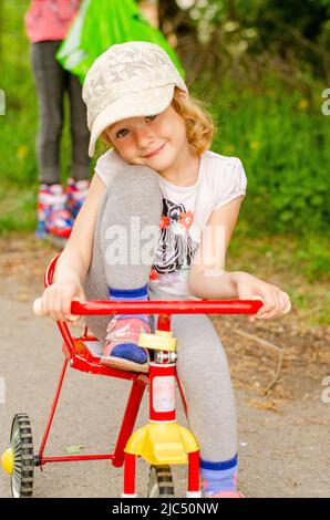 Kleines Mädchen mit einem Dreirad im Park Stockfoto