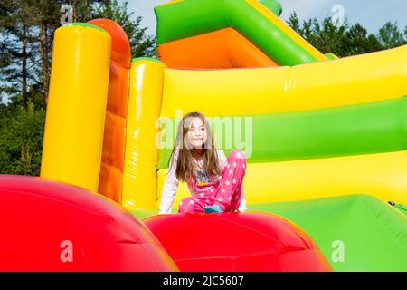Glückliches kleines Mädchen auf einer springenden Burg, ruht sich aus, während der Sprung von Ball zu Ball am sonnigen Tag. Stockfoto