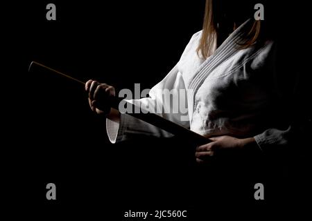 Ein Mädchen in schwarzem Hakama, das in kämpfender Pose mit Holzschwert auf dunklem Hintergrund bokken steht. Geringe Schärfentiefe. SDF. Stockfoto