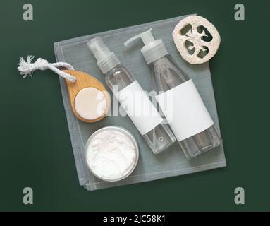 Hausgemachte Kosmetik in Plastikgläsern und Flaschen auf grauem Handtuch Draufsicht auf dunkelgrün. Modell der Markenverpackung. Bio-Naturkosmetik für Haut und ha Stockfoto