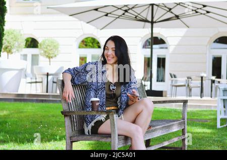 Porträt einer jungen glücklichen Geschäftsfrau, die sich in der Stadt entspannt, im Café im Freien. Kaffee trinken. Über Telefon. Selfie.-Technologie. Soziale Medien. Videoanruf. Summe Stockfoto