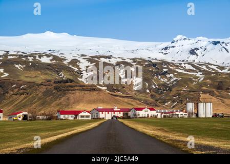 Straße, die in Richtung Thorvaldseyri Farm führt, dem Gehöft direkt vor dem Eyjafjallajökull Gletscher und Vulkan mit seinem schneebedeckten Gipfel, Island Stockfoto