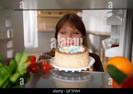 Eine junge Frau nimmt einen leckeren Kuchen aus dem Kühlschrank Stockfoto